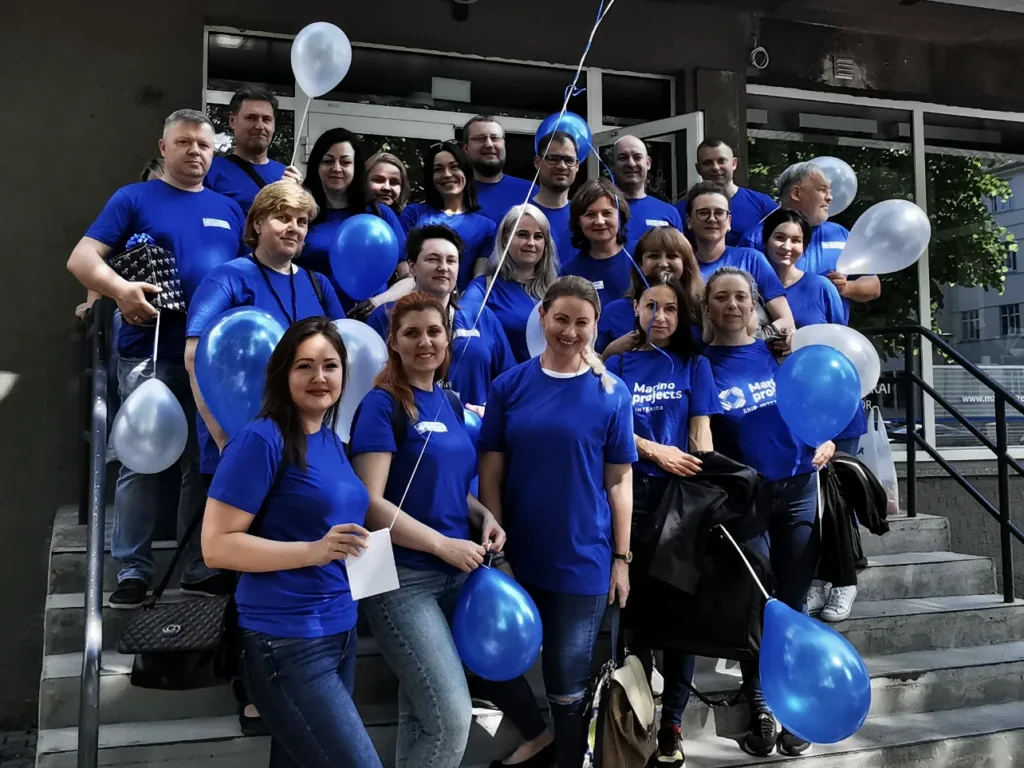 Équipe du bureau MARINO en T-shirts bleus avec des ballons devant les bureaux de l'entreprise, l'une des premières photos d'équipe